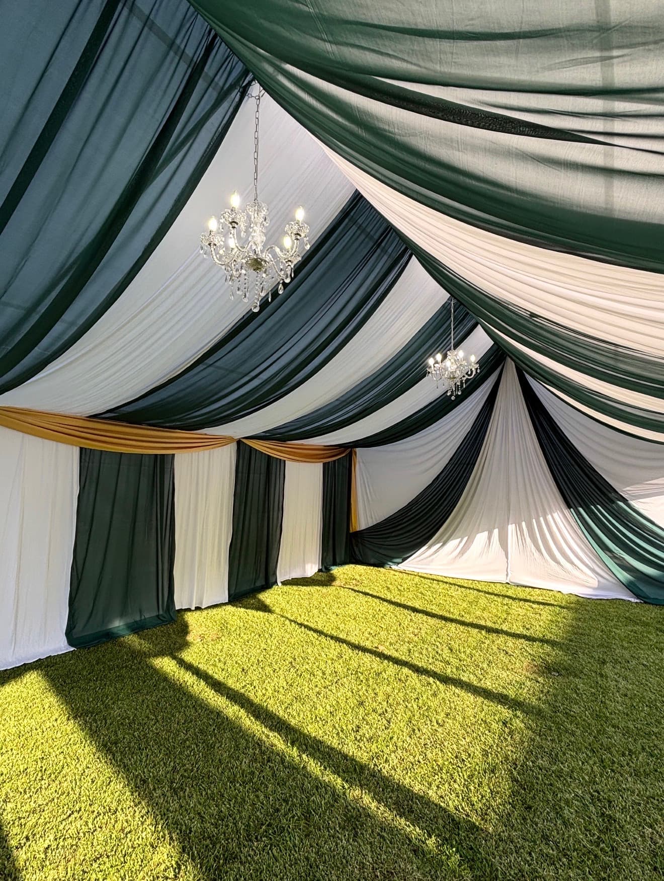 Tent interior draped in green and white panels with crystal chandeliers